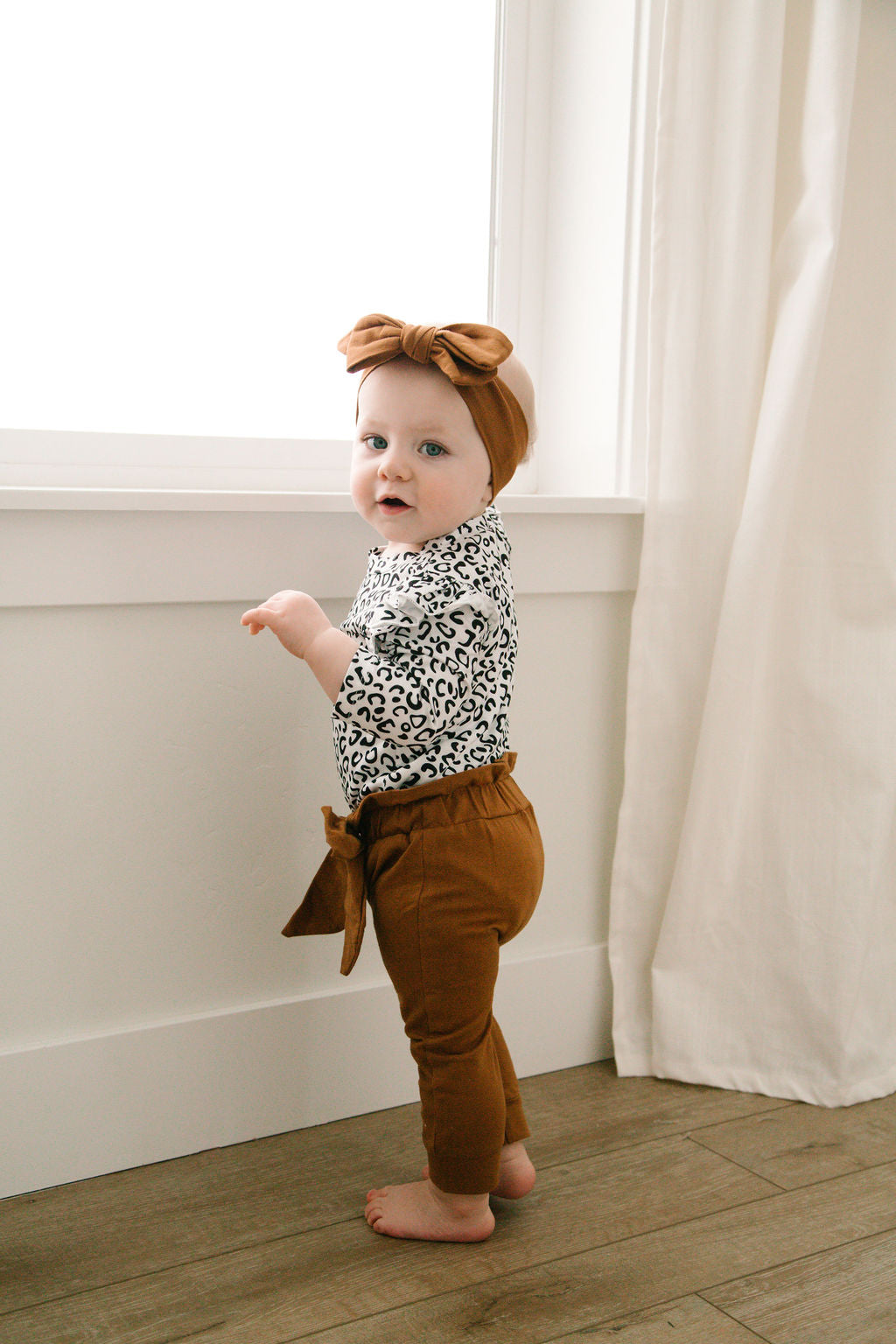 3 piece baby girl leopard printed bodysuit with ruffle shoulders & snaps. Rust pants with matching headband.